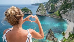 Young woman making heart shape to dreamlike beach from above - Blues and green sand the beautiful mountain shaped on the sea.Travel destinations vacations love people wonderlust concept nature scenics